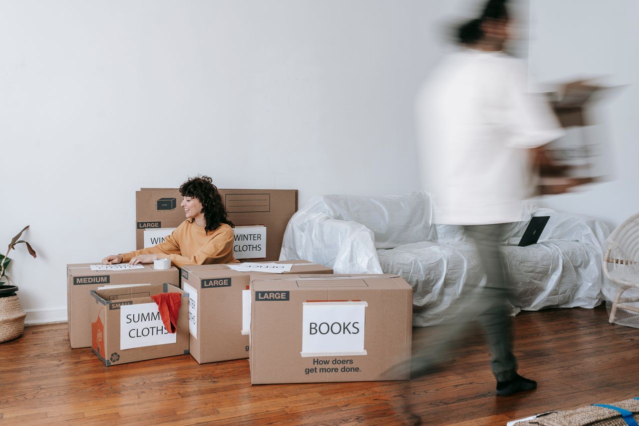 about-us A couple packing labeled boxes in a minimalist living room, preparing for moving day.